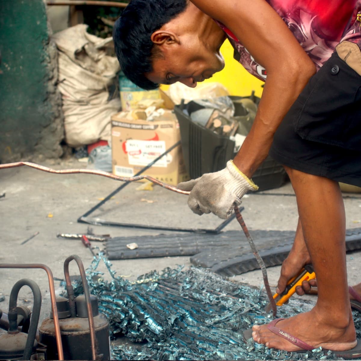A wasteworker recovers the copper piping off a heat exchanger. Using only a cutter, he separates the metallic fins from the copper pipes, sending metallic dust into his face. (Alex Lauricio/Philippine Collegian)
